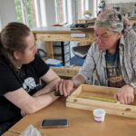 Maker and supervisor measuring a wooden box.